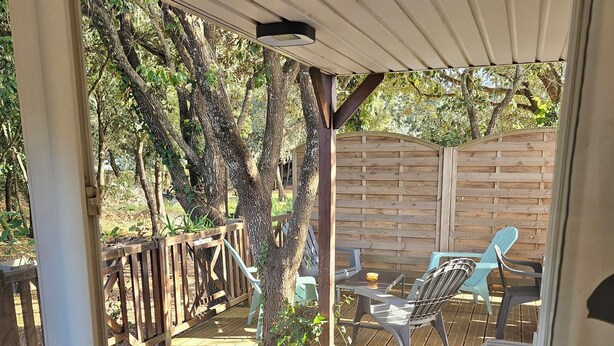 A wooden deck with a covered seating area, a wooden fence, and a tree. - Quiet chalet under the trees 3 km from Bonifacio and 2 km from the beaches (Bonifacio)
