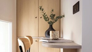 Un pequeño comedor con dos sillas de madera, una mesa, un florero con hojas verdes y un interruptor de luz en la pared.
