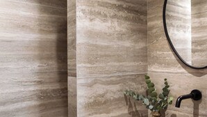 Un baño moderno con pared de mármol, un lavamanos redondo, un grifo negro y un cabezal de ducha.