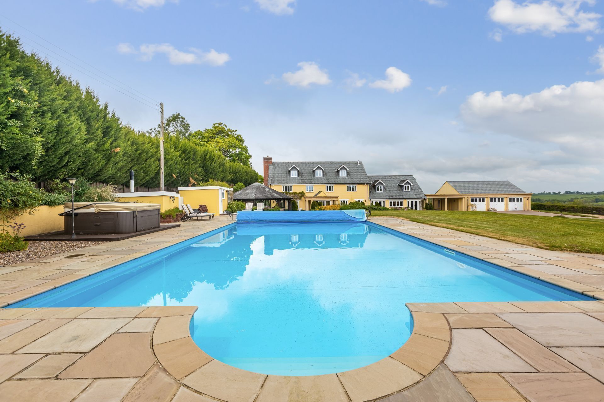 A rectangular swimming pool with a tiled deck, surrounded by a grassy area and a row of houses.