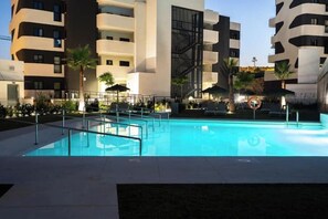 Un hotel moderno con piscina, zona de estar al aire libre y área de piscina bien iluminada.