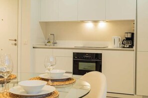 Una cocina moderna con armarios blancos, horno empotrado y cafetera.