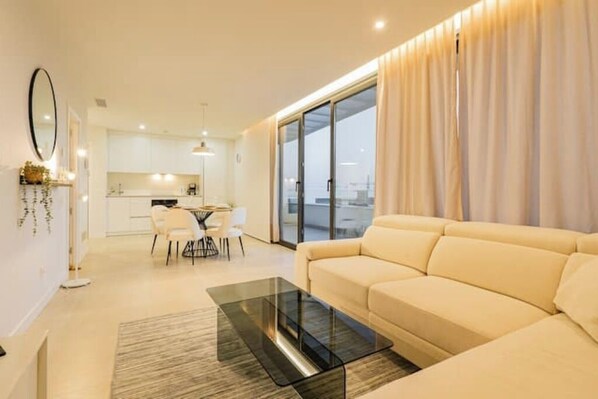 Una sala de estar moderna con un sofá, una mesa de centro de vidrio y un comedor con sillas y una mesa.