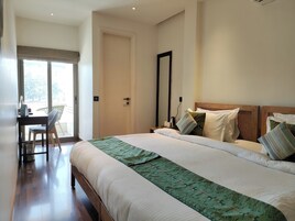Quarto de hotel com uma cama grande, uma escrivaninha com cadeira, um espelho e vista através de uma porta.