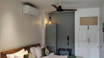 A bedroom with a bed, a ceiling fan, an air conditioning unit, a wardrobe, and a bedside table.