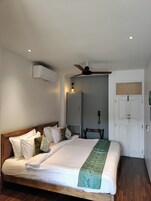 A bedroom with a bed, a ceiling fan, an air conditioning unit, a wardrobe, and a bedside table.