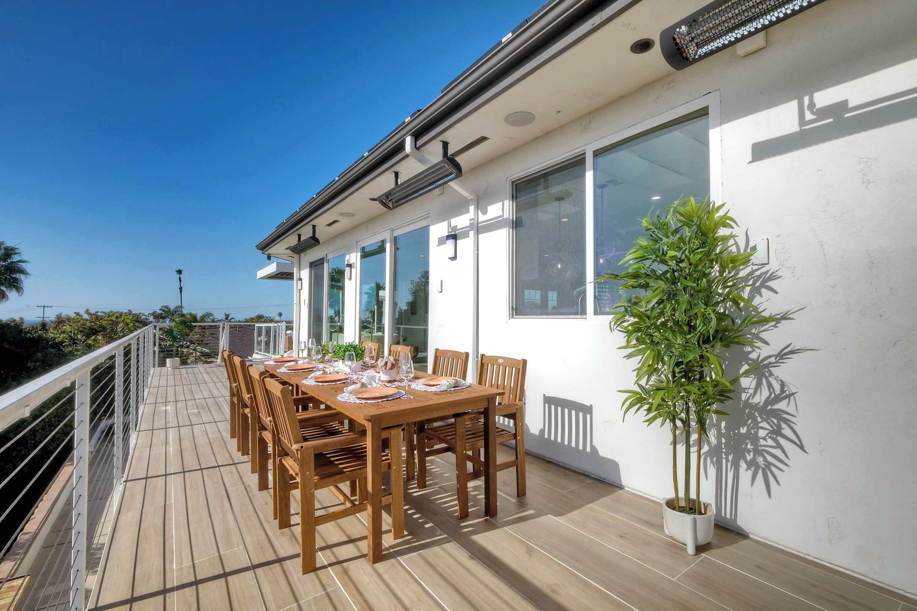 Una terraza de madera con una mesa lista para comer, ventanas amplias y una planta en maceta.