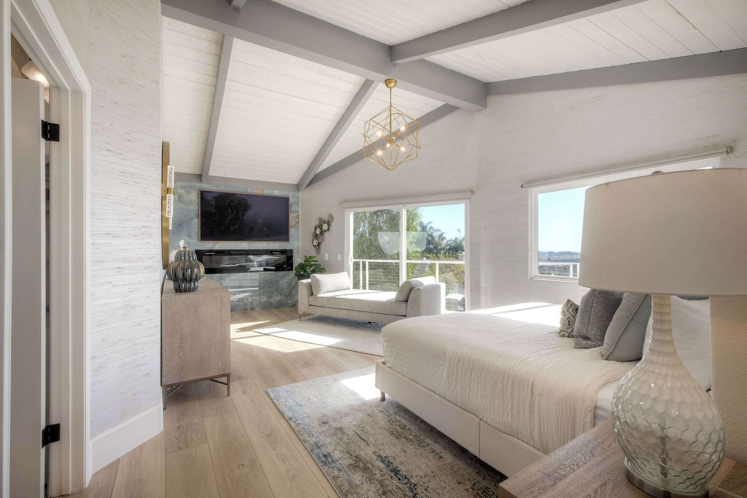 A bedroom with a large bed, a TV mounted on the wall, a window with a view, and a ceiling with exposed beams.