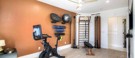 Un gimnasio en casa con equipo de ejercicio, un ventilador de techo y una escalera de madera.