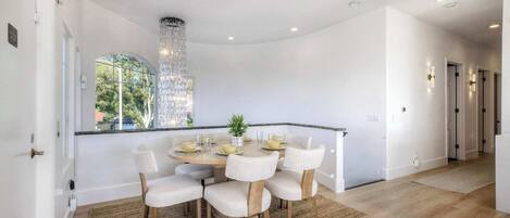 A dining area with a round table, six chairs, and a chandelier.