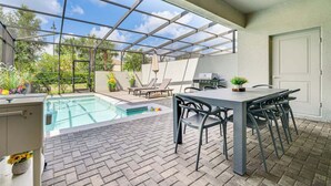 Ein überdachter Außenbereich mit Pool, Esstisch, Stühlen und Grill.