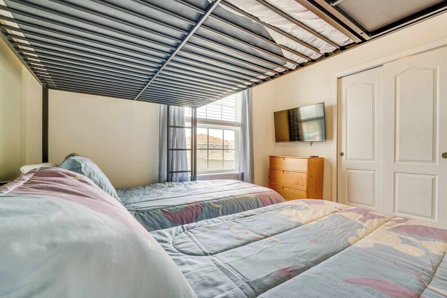 A bedroom with two beds, a wooden dresser, a TV, and a window with curtains.