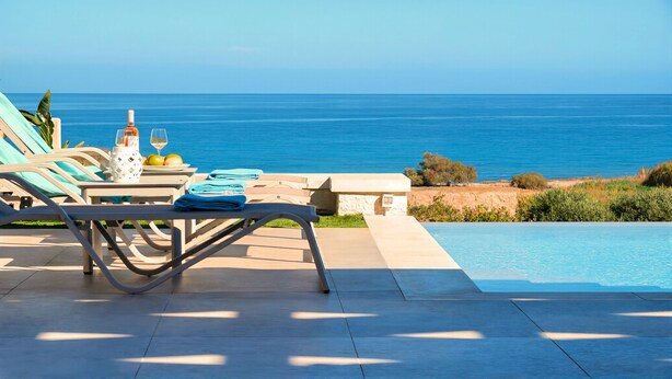 A poolside area with lounge chairs, a table with a bottle and glasses, and a view of the sea. - Vista Mare Gold Villa Heated Pool (Dramia)
