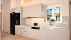 A modern kitchen with white cabinetry, a black refrigerator, a built-in oven, a dishwasher, and a window with a view of the outdoors. - Vista Mare Gold Villa Heated Pool (Dramia)