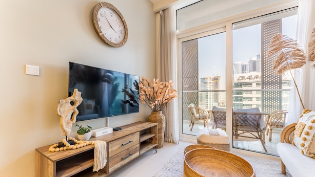 Un salon moderne doté d’un téléviseur à écran plat, d’un meuble de rangement en bois et d’une grande fenêtre offrant une vue sur la ville.