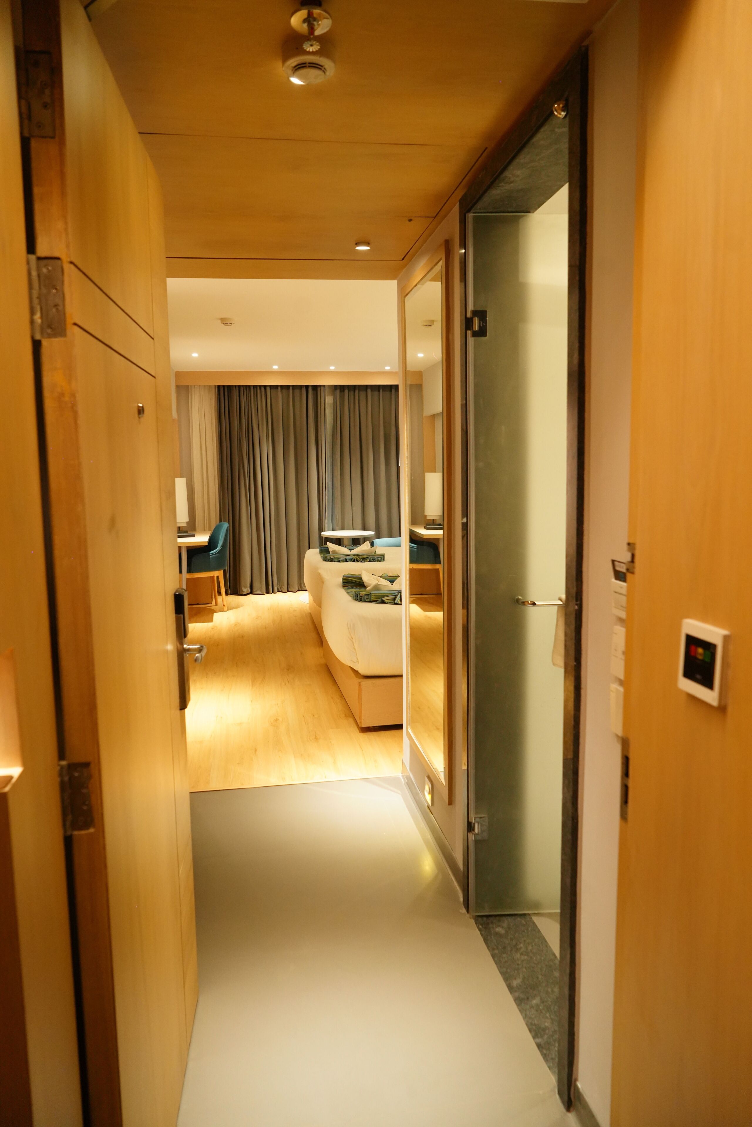 A hotel corridor with a bed, a desk, and a chair in the room.