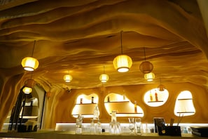 Habitación con un diseño de techo ondulado único, iluminación colgante y una zona de bar con estantes y cristalería.