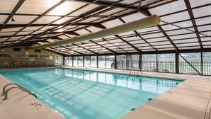 Piscina interior com cobertura metálica e paredes de vidro, cercada por uma área vedada.