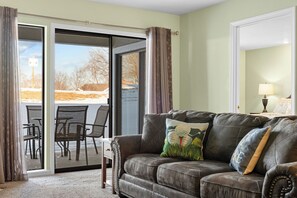 A living room with a leather sofa, a glass door leading outside, and a table with chairs. - Walk-In 2BR | Golf View | No Stairs | Pools (Branson)