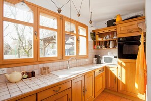 Une cuisine avec des meubles de rangement en bois, un évier, une cuisinière et une fenêtre donnant sur un jardin.