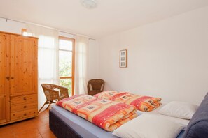Une chambre à coucher avec un lit, une armoire en bois, une chaise et une fenêtre avec des rideaux.