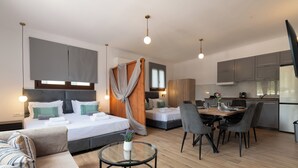 A modern hotel room with a bed, a sofa, a dining table with chairs, a kitchen area, and a TV. - Anthi Luxury Residence- Jasmine (Ialisos)