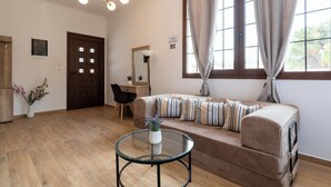 A living room with a sofa, a glass coffee table, a wooden floor, a door, and a window with curtains. - Anthi Luxury Residence- Jasmine (Ialisos)