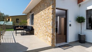 A modern building with a stone facade, a patio with outdoor furniture, and a potted tree. - Anthi Luxury Residence- Jasmine (Ialisos)