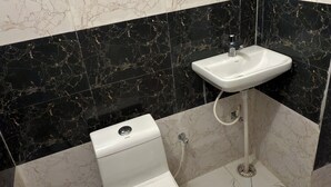 A bathroom with a toilet, sink, and mirror. - Gulmohar Stays (siddhagiribagh)