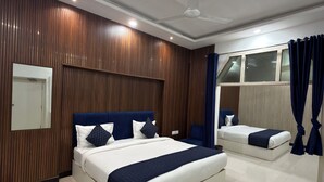 A modern hotel room with a large bed, a smaller bed, a ceiling fan, and a window with curtains. - Gulmohar Stays (siddhagiribagh)