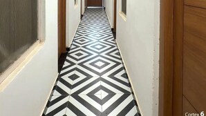 A hallway with patterned flooring, white walls, and wooden doors. - Gulmohar Stays (siddhagiribagh)