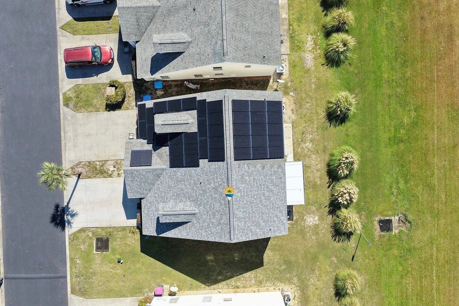 Een woongebouw met een schuin dak, zonnepanelen en een kleine tuin met palmbomen.