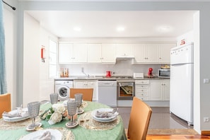 A modern kitchen with white cabinets, a dining table set with glassware and plates, and a red kettle. - Lobos Village (Câmara de Lobos)