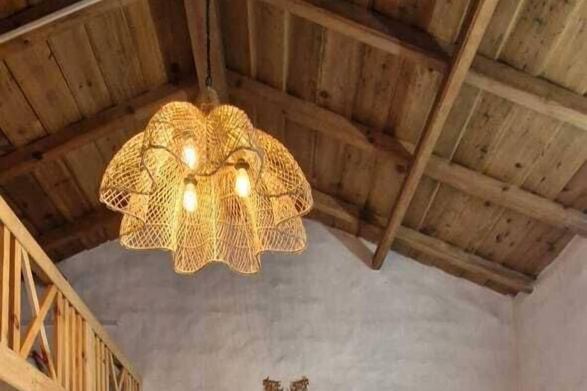 Una camera da letto con soffitto in legno, un letto con copriletto rosso e floreale, un tappeto blu decorato e una TV montata a parete.