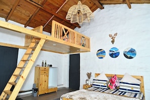 Une chambre à coucher aménagée dans un espace en hauteur, avec une échelle en bois, un lit superposé et un luminaire suspendu.