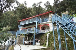 A multi-story building with a red roof, blue railings, and a staircase leading to the upper levels. - Tatsaaraa Kavan (Ramgarh)