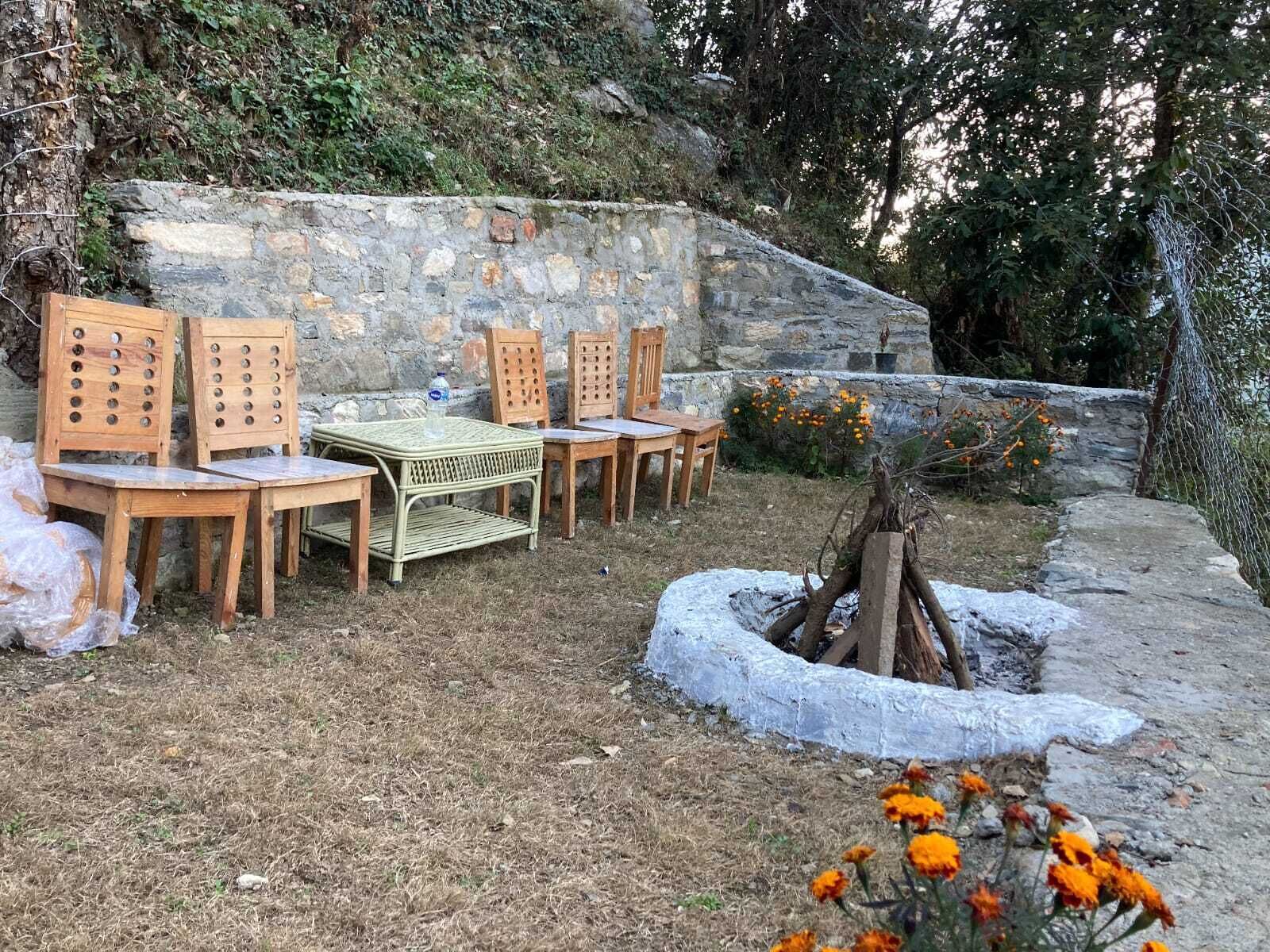 An outdoor seating area with a stone wall, wooden chairs, a table, and a fire pit.