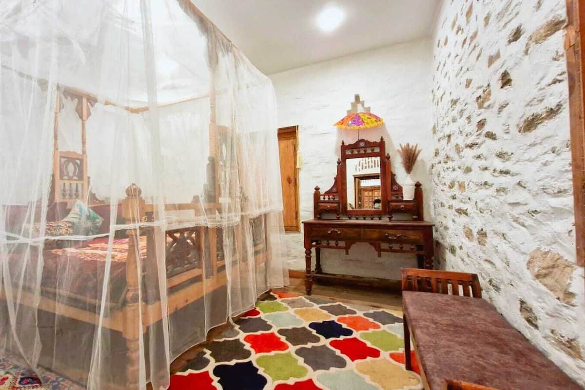 Una stanza con un letto coperte da zanzariera, un comò in legno e un tappeto decorato.