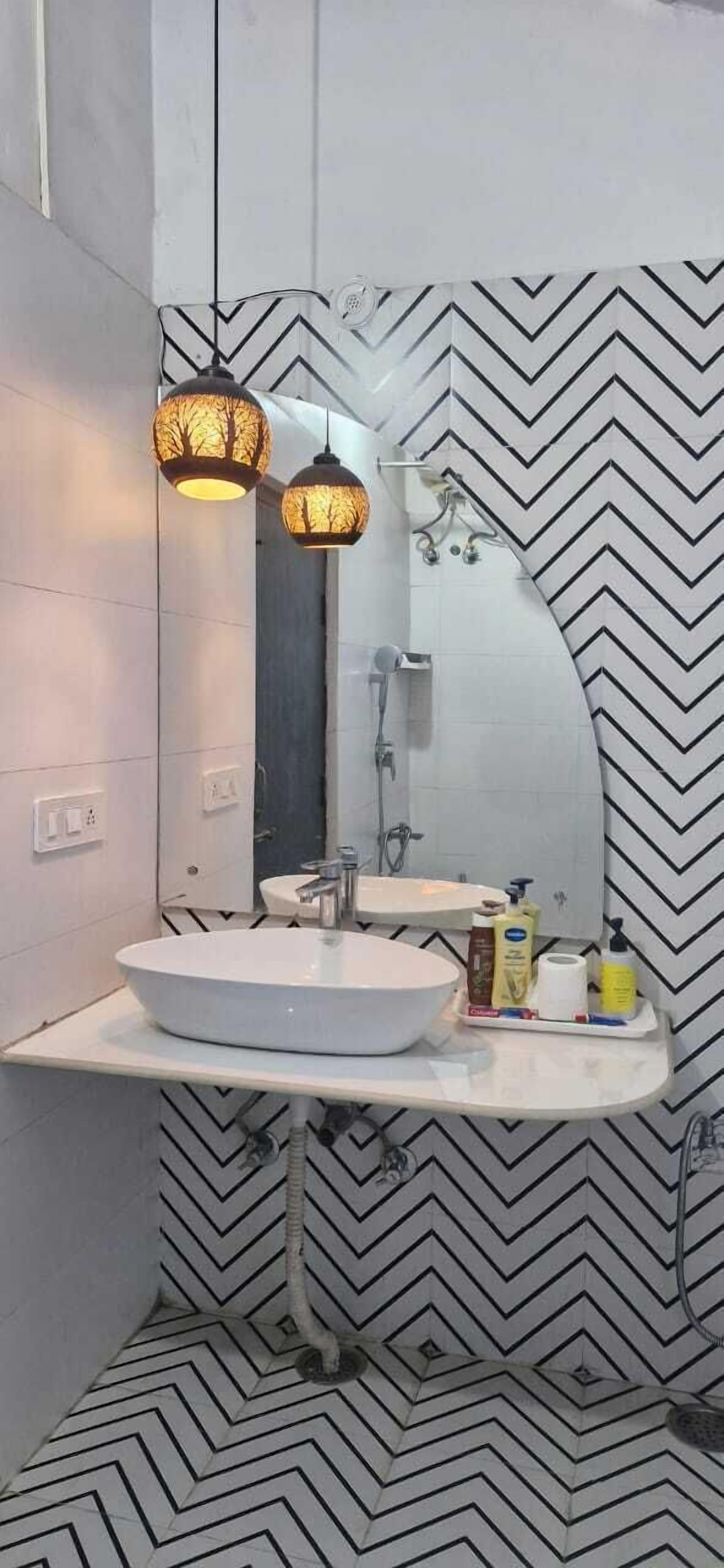 Ein modernes Badezimmer mit einem weißen Waschbecken, einem Spiegel und zwei Pendelleuchten mit Baummotiven.
