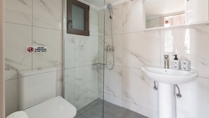 Un baño moderno con ducha envuelta en vidrio, un lavabo blanco y dispensadores de jabón tipo mármol, y un inodoro.