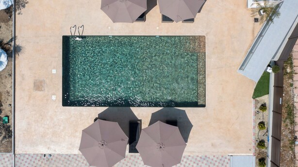 Vista aérea de una piscina rectangular con agua cristalina, rodeada por un solárium con baldosas.