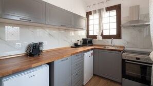 Una cocina moderna con armarios grises, encimera de madera, lavavajillas integrado, estufa y ventana con cortinas.