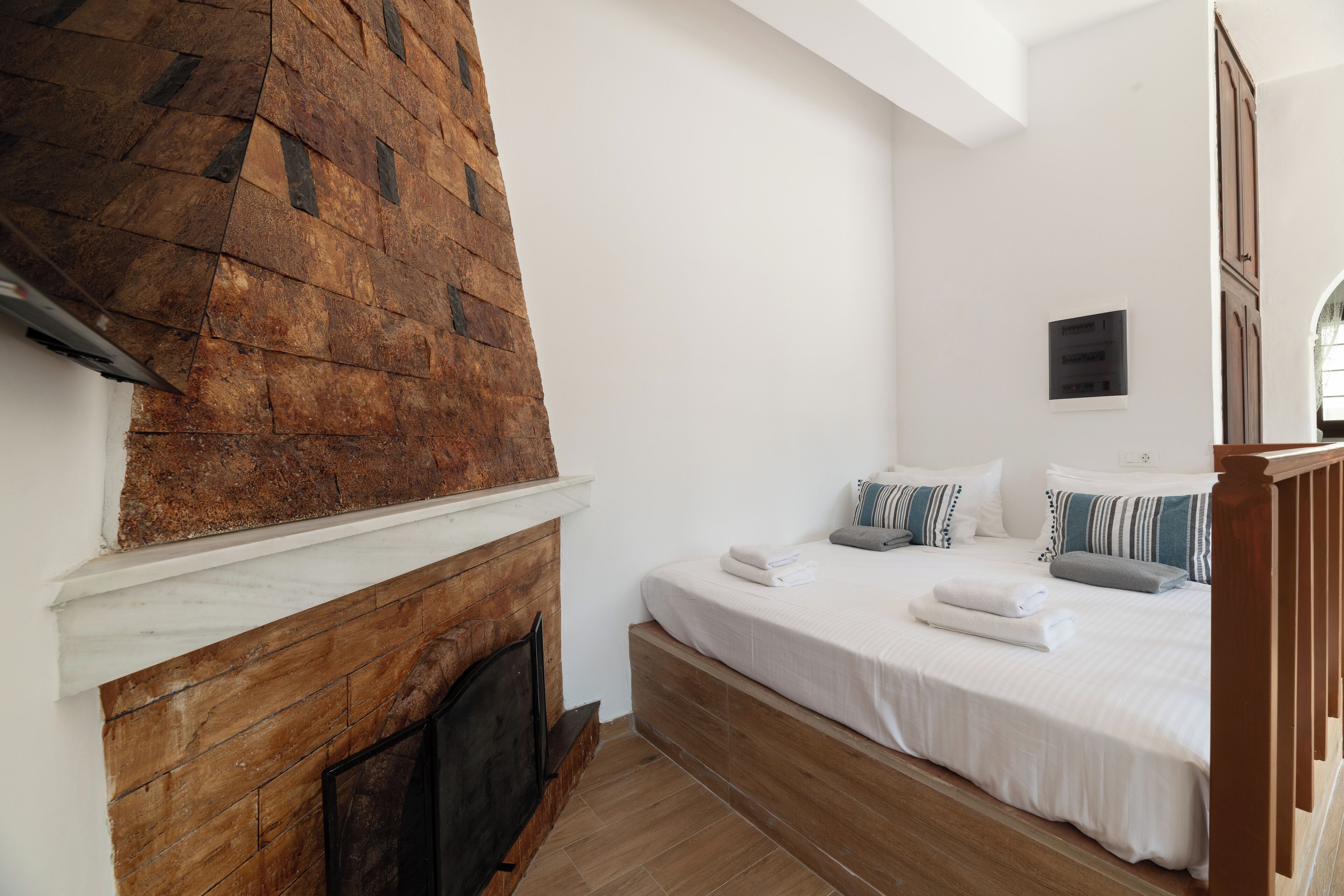 A bedroom with a fireplace, a bed with pillows, and a wooden headboard.