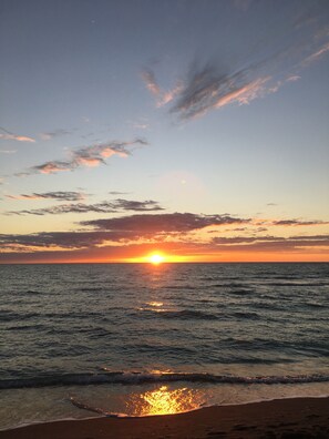 Solnedgang over et roligt hav med en strand i forgrunden.