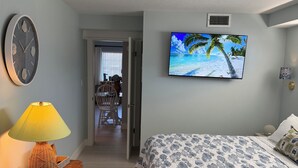 Een slaapkamer met een bed, een televisie aan de muur, een klok en een lamp op een dressoir.