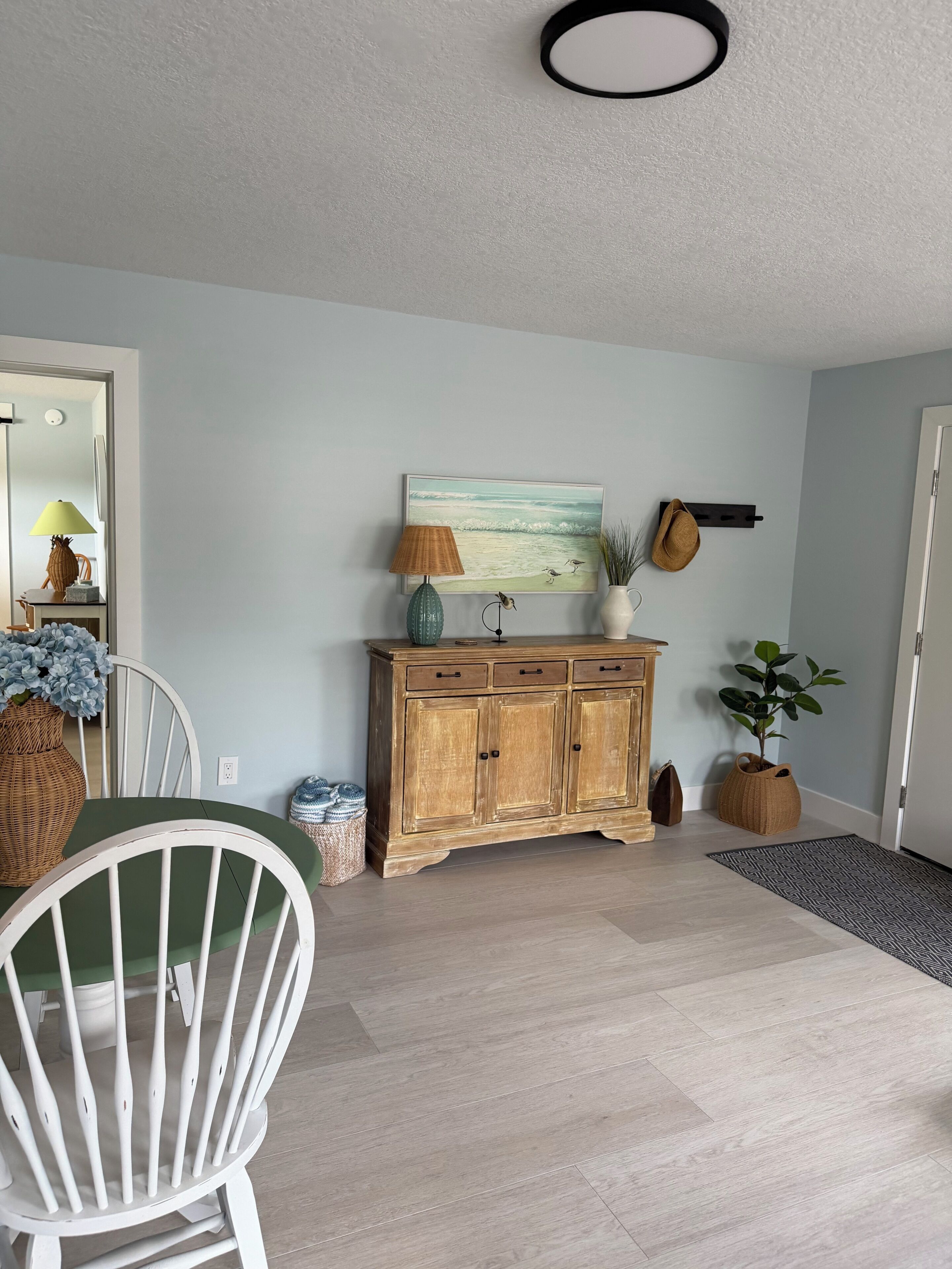 A dining area with a wooden cabinet, a painting, and a potted plant.