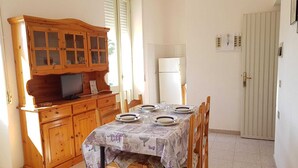 Zona pranzo con un armadietto in legno, una televisione e un tavolo imbandito per quattro persone.