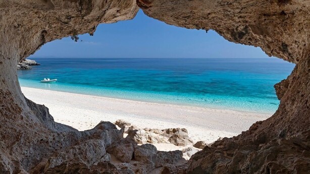 Vista di una spiaggia attraverso l'ingresso di una grotta rocciosa, con una barca sull'acqua.