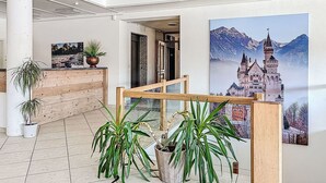 Eine geräumige Lobby mit einem hölzernen Empfangsschalter, Blumentöpfen und einem großen Landschaftsgemälde eines Schlosses.
