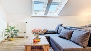 A modern living room with a sectional sofa, a wooden coffee table, a potted plant, and a skylight above. - Beautiful apartment for 3 people with WIFI, TV and pets allowed (Klausmen)